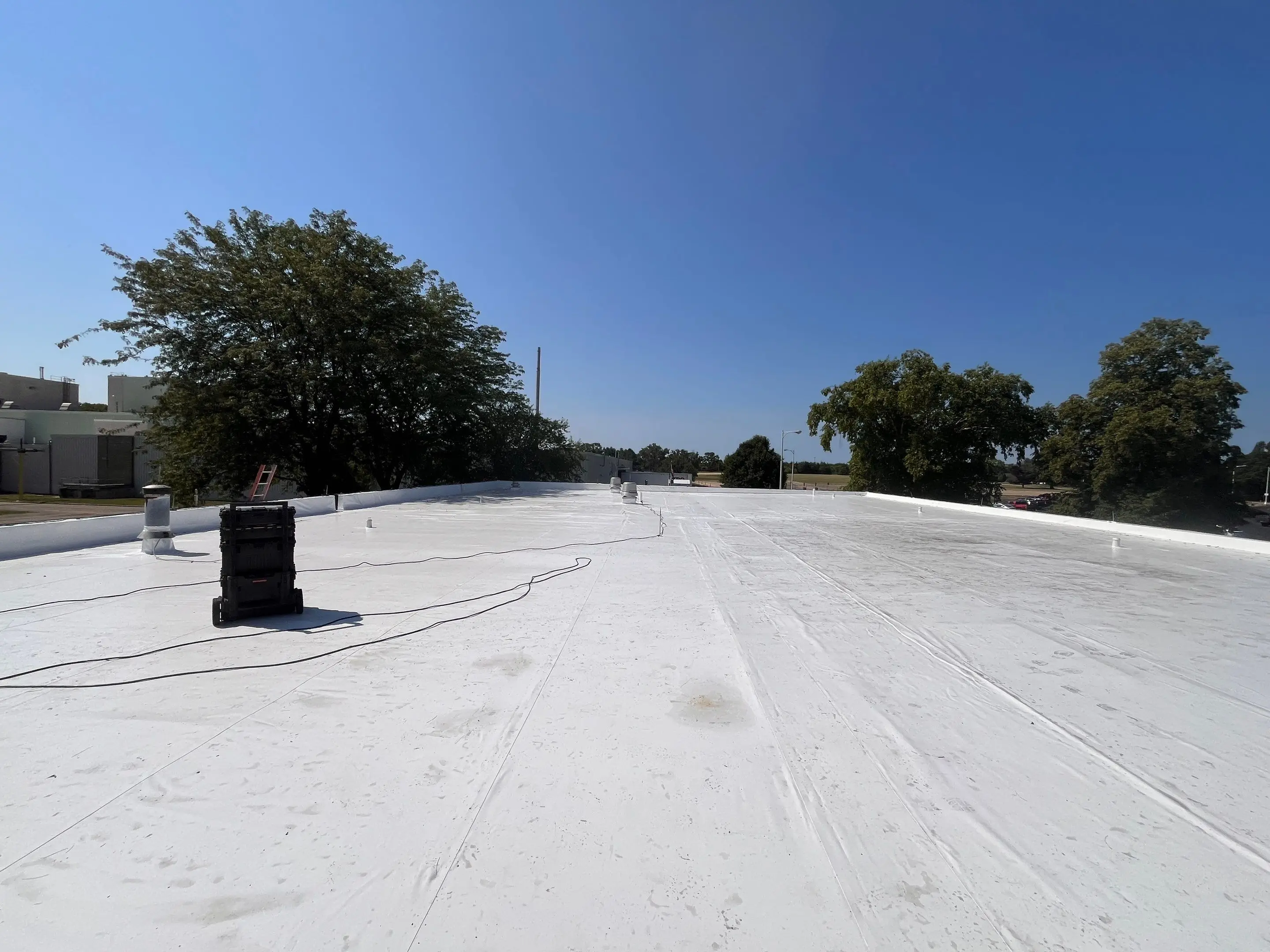 New white Duro-Last roof on a manufacturing office building in Camanche, Iowa, with trees behind